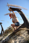 Boy playing pirate at a rosty anchor on beach, Ilha de Tavira, Tavira, Algarve, Portugal