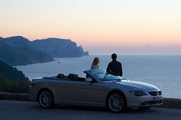 Couple with car on coastal road, North Coast, Majorca, Spain