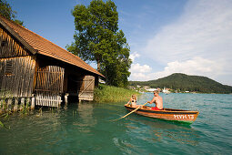 Couple in a rowboat leaving a boathouse, Lake Faak, Carinthia, Austria