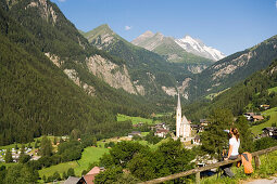 Frau rastet nach eine Wanderung, Heiligenblut mit Wallfahrtskirche Zum heiligen Blut, Blick zu Grossglockner, Heiligenblut, Kärnten, Österreich