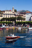 View over Lake Lugano to Luganow with cathedral St. Lorenzo, small motorboat in foreground, Lugano, Ticino, Switzerland