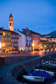 Harbour and harbour promenade with spire of church Santi Pietro Paolo in background in the evening, Ascona, Lake Maggiore, Ticino, Switzerland