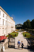 Tourists strolling through Mirabell garden, Hohensalzburg Fortress, largest, fully-preserved fortress in central Europe, in background, Salzburg, Salzburg, Austria