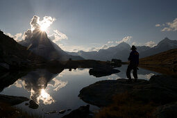 Person watching sunset, east side (Hörnligrat) of Matterhorn (4478 m) reflected in Riffelsee, Zermatt, Valais, Switzerland