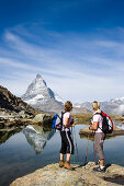 Two female hikers looking at the reflection of the east face, Hoernligrat, of the Matterhorn, 4478 m, in Riffelsee, Zermatt, Valais, Switzerland