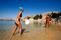 Couple playing beach pingpong, standing in shallow water, Saint Paul's Bay (Agios Pavlos), Lindos, Rhodes, Greece
