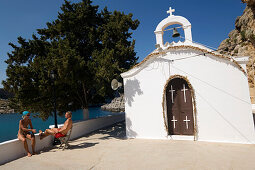 Couple sitting in front of Saint Paul's Chapel, Saint Paul's Bay (Agios Pavlos), Lindos, Rhodes, Greece