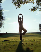 Frau entspannt in einer Yogaübung auf Wiese im Park eines Wellnesshotels, Abendsonne, bei Hameln, Weserbergland, Niedersachsen, Deutschland