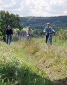 J unge, sportliche Familie mit Sohn, Fahrradtour auf einem Wiesenweg, im Hintergrund das Schloßhotel Münchhausen, bei Hameln, Weserbergland, Niedersachsen, Deutschland