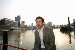 Young business man sitting in front of the Media Harbour, state capital of NRW, North Rhine-Westphalia, Germany