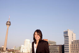 Young business woman in front of city skyline, Media Harbour Düsseldorf, with television tower, Zollhof, architecture of Frank O.Gehry, Düsseldorf, state capital of NRW, North-Rhine-Westphalia, Germany