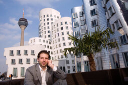 Young business talking on his mobile phone in front of the Neuer Zollhof, modern architecture from Frank Gehry, with television tower in the background, Media Harbour, Düsseldorf, state capital of NRW, North-Rhine-Westphalia, Germany