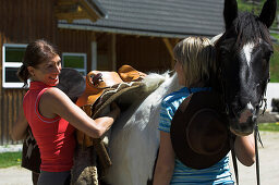 Two women saddling a horse at stables, Muehlviertel, Upper Austria, Austria