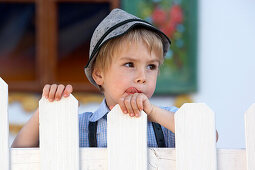 Boy (3-4 years) standing behind a fence