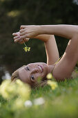 Junge Frau liegt auf einer Blumenwiese und lächelt in die Kamera, Icking, Bayern, Deutschland