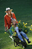 Young woman pushing friend sitting in hand barrow, Brannenburg, Upper Bavaria, Bavaria, Germany