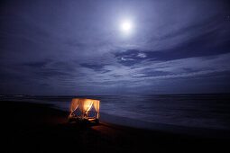 Illuminated four-poster bed standing on the beach at night, Bali, Indonesia