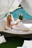 A young woman reading a book, resting on a sun lounger near the pool, near Uluwatu, Bali, Indonesia