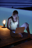 Junge Frau sitzt mit Laptop am Pool, nahe Uluwatu, Bali, Indonesien