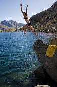 Young woman jumping into lake Lago d'Orsino, Gotthard, Canton of Ticino, Switzerland