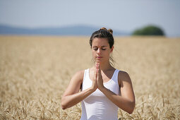 Frau mittleren Alters meditiert in einem Getreidefeld