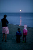 Mother and children at the beach, full moon rising over Golden Bay, northern coast of South Island, New Zealand