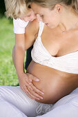 Boy's (4-5 years) hand resting on pregnant mother's hand on belly, Styria, Austria