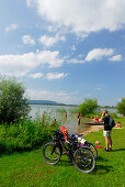 Badegäste mit Fahrrädern am Ufer des Kochelsees und Mann mit Handy, Oberbayern, Bayern, Deutschland