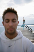 Mann mit geschlossenen Augen, Frau beim Yoga auf Steg am Starnberger See, Münsing, Bayern, Deutschland, MR