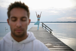 Mann mit geschlossenen Augen, Frau beim Yoga auf Steg am Starnberger See, Münsing, Bayern, Deutschland, MR