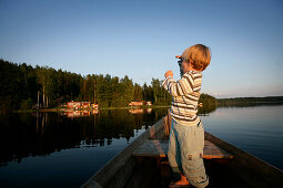 Boy standing up in a rowing boat on a lake, Lake Nossen, Vimmerby, Smaland, Sweden