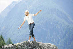 Frau balanziert barfuß auf Felsen, Heiligenblut, Nationalpark Hohe Tauern, Kärnten, Österreich