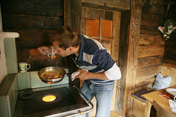 Mann kocht Rührei in einer Almhütte, Heiligenblut, Nationalpark Hohe Tauern, Kärnten, Österreich