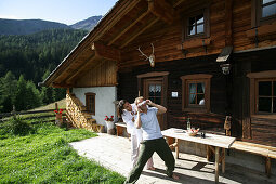 Couple playing blindman's buff beside alp lodge, Heiligenblut, Hohe Tauern National Park, Carinthia, Austria