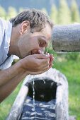 Man drinking water from a font, Heiligenblut, Hohe Tauern National Park, Carinthia, Austria