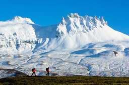 Two hikers passing snow covered mountain range, Iceland