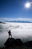 silhouette of hiker standing on rock high above fogbank in Upper Engadin, Piz Julier, Engadin, Grisons, Switzerland
