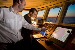 Captain and helmsman in training on the bridge of a ship, Hanse Explorer, in the evening light, Great Britain