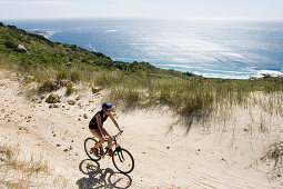 Mountainbikerin fährt entlang der Sandy Bay, Kaptstadt, Südafrika