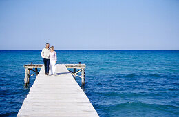 Couple sitting walking in a wooden footbridge over the sea