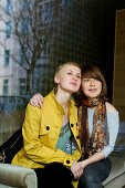 Two young woman sitting on a sofa while looking out of a window, Düsseldorf, North Rhine-Westphalia, Germany