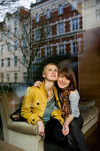 Two young woman sitting on a sofa while looking out of a window, Düsseldorf, North Rhine-Westphalia, Germany