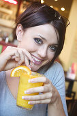 21 year old girl in restaurant drinking a glass of fresh orange smiling into camera