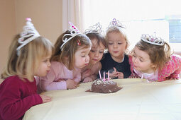 group of 3, year old girls at a party, blowing the candle out on a birthday cake