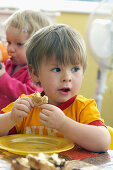 3 year old boy , looking off camera, at nursery, eating his dinner