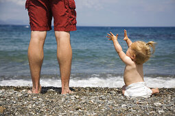 Daughter and father looking out into the ocean on a gravel beach in Kos Island. Greece. Daughter reaching for father