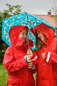 Two girls (6-7 years) wearing rainwear under an umbrella, Upper Bavaria, Germany
