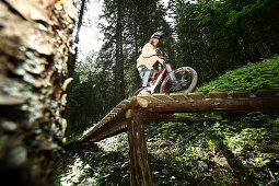 Mountain biker riding over a ramp in a forest, Oberammergau, Bavaria, Germany