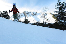 Snow-shoeing young man with a snowboard, Reutte, Tyrol, Austria