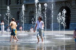 Children playing in the trick fountains and water gardens in front of the House of Parliament on Parliament Square, Bundeshaus, Bundesplatz, Old City of Berne, Berne, Switzerland